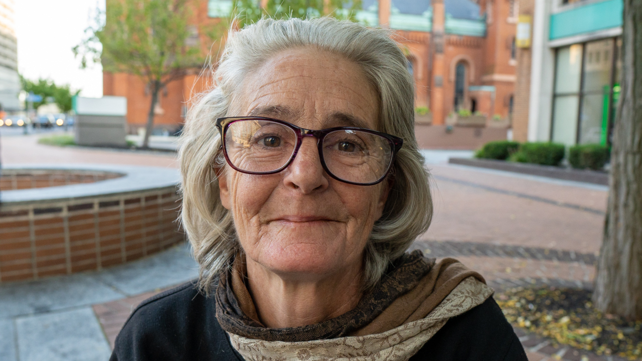 Portrait of an older homeless woman wearing glasses standing outside.