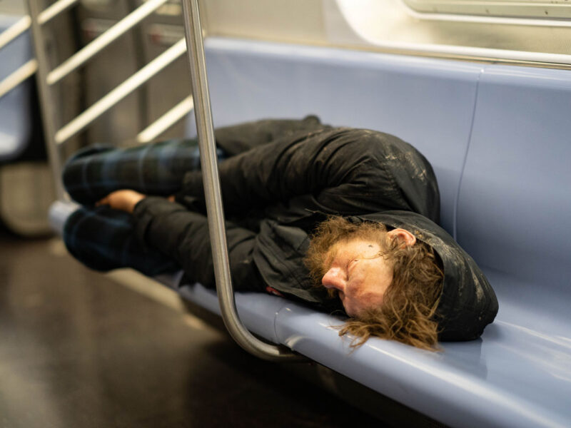 a homeless man sleeps on a NYC subway bench during Coronavirus