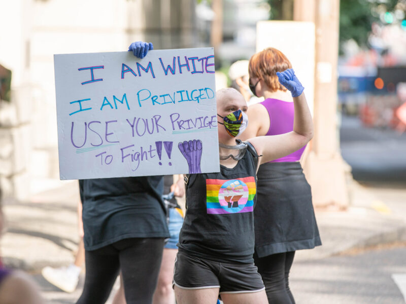 White protester holds sign telling white people to use their privilege to help people of color